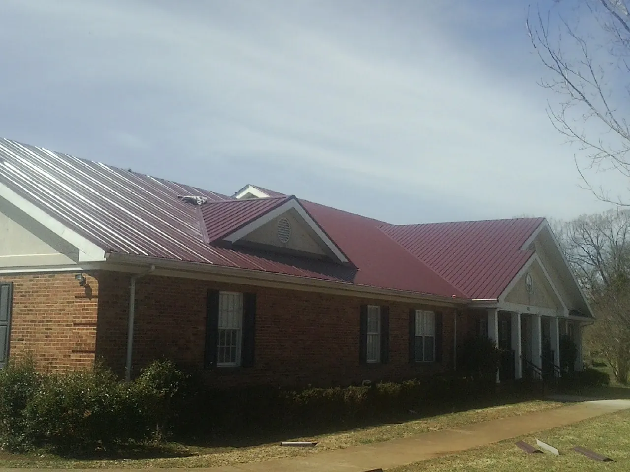 Red metal roof with gabled entries on a long brick building, from a Hail Damage Roof Repair job in Riverton