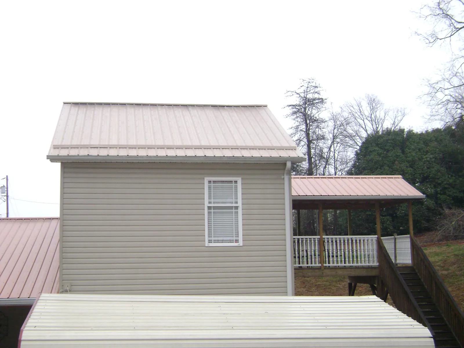 Tan metal roofs on a two story addition and attached porch, from a Roof Replacement job in Riverton
